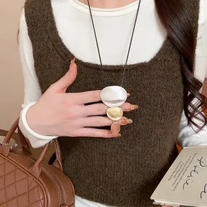Close-up of minimalist geometric metal sweater necklace with tri-color oval pendants