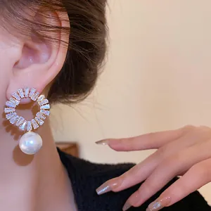 Nahaufnahme von Blumenohrringen mit Baguette-Diamanten und einem weißen Perlenanhänger.