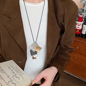 Close-up view of geometric metallic square pendants on a layered sweater necklace.