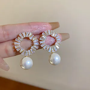 Nahaufnahme von eleganten Goldohrringen mit funkelnden Kristallen und weißer Perle.