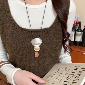 Detailed view of a long geometric tri-color metal pendant necklace on a brown knit vest.