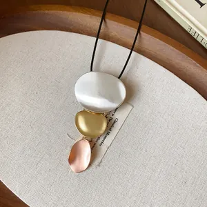 Macro detail of three-tone metallic geometric pendants on a minimalist black cord necklace.