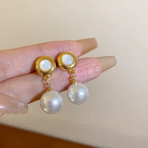Nahaufnahme eleganter goldener Perlenohrringe mit runden Steckern, in der Hand gehalten.