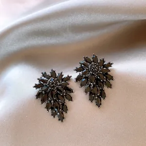 Macro detail of elegant black crystal flower stud earrings resting on luxurious champagne silk