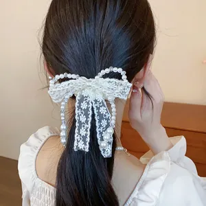 Close-up view of elegant white lace bow hair tie with pearls and beads on low ponytail