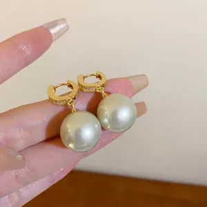 Detailansicht eleganter goldener Creolen mit großen runden Perlen und Strasssteinen.