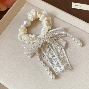 Detailed view of an elegant cream lace bow hair scrunchie with pearl beads and satin texture.