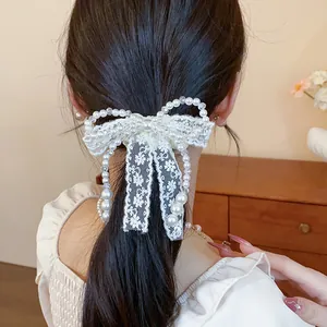 Detail view of an elegant white lace bow hair tie decorated with pearls and clear beads.