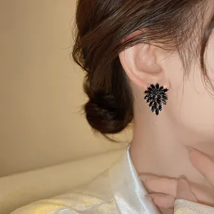Close-up of elegant black flower stud earrings with rhinestones worn by a model.