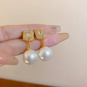 Detailansicht eleganter goldener Ohrstecker mit Diamanten und großen Perlenanhängern.