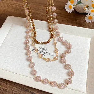 Dettaglio di una collana a più strati con perle di vetro rosa e perle di cristallo lucide.