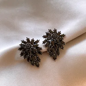 Close-up detail of exquisite black flower-shaped zircon stud earrings on beige satin fabric
