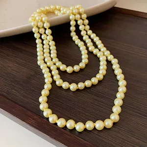Detailed close-up of an elegant long cream pearl necklace draped on a dark wooden surface.