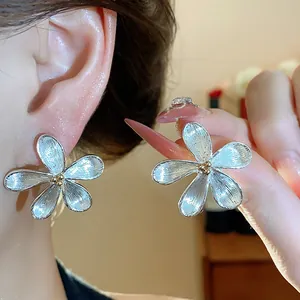 Gros plan de boucles d'oreilles fleurs en argent avec texture brossée et centre doré.