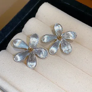 Détail macro de boucles d'oreilles fleurs en argent avec texture brossée et centre doré