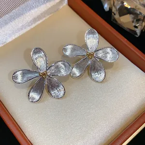 Gros plan sur des boucles d'oreilles fleur argentées avec texture en métal brossé.