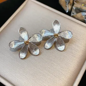 Gros plan de boucles d'oreilles fleurs argentées avec texture brossée et cœur doré.