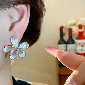 Gros plan d'une boucle d'oreille fleur argentée avec une texture de métal brossé