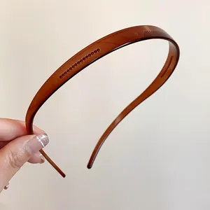 Une main tenant un serre-tête en acrylique marron minimaliste avec dents antidérapantes.