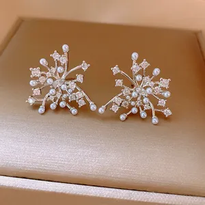 Macro detail of snowflake stud earrings featuring white pearls and sparkling rhinestones.