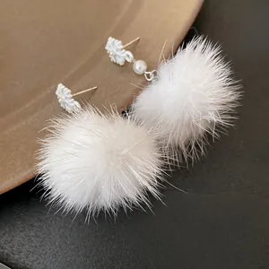 Close-up detail of white snowflake earrings featuring soft fur balls and elegant pearls.
