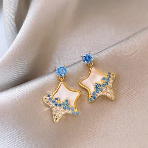 Detailed close-up of gold-plated star earrings with blue and white crystals.