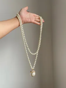 Vista dettagliata di una collana di perle a due fili con un grande pendente di strass in mano.