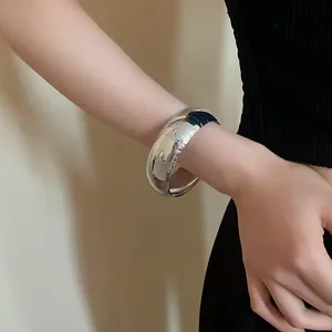 Primo piano di un ampio bracciale a fascia in metallo argentato con texture a coccodrillo