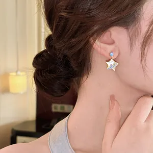 Detail of a star-shaped resin earring with blue rhinestones worn on a female model's ear