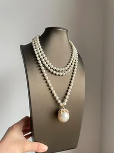 Dettaglio ravvicinato di una collana di perle a tre strati con grande ciondolo lucido.