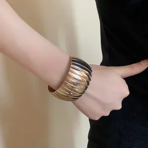 Dettaglio ravvicinato di un audace bracciale rigido in metallo dorato a coste su un polso