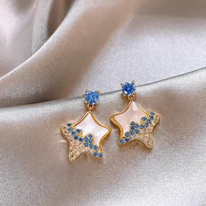Elegant gold star stud earrings with blue and white crystals on silk background