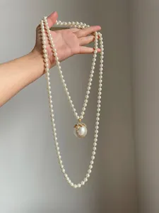 Elegante collana lunga di perle con grande ciondolo di strass tenuta in mano