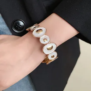 Vista dettagliata di un bracciale dorato vintage con segmenti ovali in smalto bianco