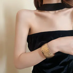 Dettaglio di un bracciale a polsino in metallo dorato testurizzato su modella