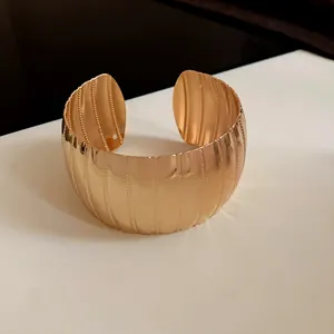 Dettaglio di un ampio bracciale rigido in metallo dorato con trama a coste sottili.