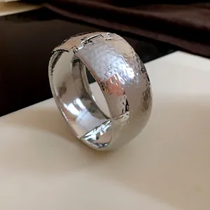Primo piano di un ampio bracciale a polsino in metallo martellato argento, stile minimale.