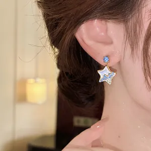 Close-up wearing view of star earrings with blue crystals and resin inlay detail