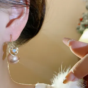 Détail de boucles d'oreilles pendantes en perles et cœur doré avec pavé de cristaux