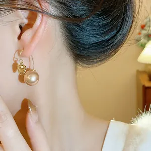 Vue rapprochée d'élégantes boucles d'oreilles cœur et perle champagne portées à l'oreille