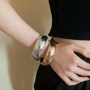 Primo piano di grossi bracciali in metallo testurizzato oro e argento indossati da una modella