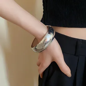 Primo piano di un ampio bracciale in metallo argento con motivo logo sul polso.