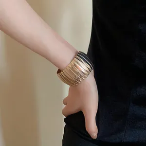 Dettaglio di un bracciale a manchette in metallo dorato a coste indossato al polso