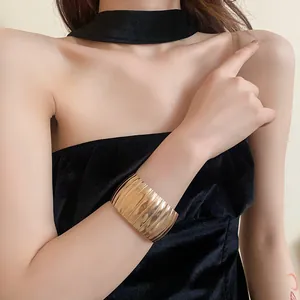Dettaglio di un ampio bracciale rigido dorato con trama a coste verticali indossato dal modello