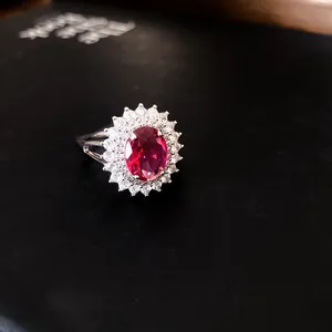 Close-up of luxury silver ring featuring a large oval red gemstone with zircon halo.