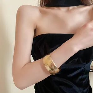 Dettaglio ravvicinato della texture martellata di un ampio bracciale rigido dorato al polso