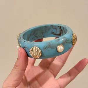 Elegante bracciale in resina blu con dettagli a conchiglia dorata e perle in mano