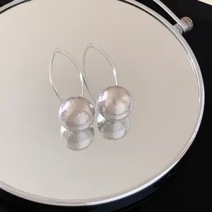 Close-up detail of brushed silver metal spherical earrings with elegant curved hooks.