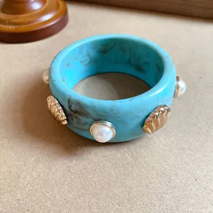 Primo piano di un bracciale rigido in resina blu marmorizzata con conchiglie e perle