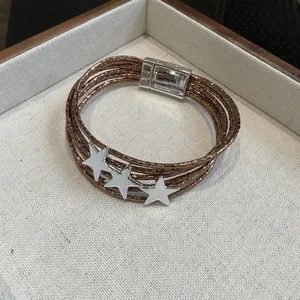 Dettaglio di un bracciale multistrato in bronzo con ciondoli a stella e chiusura magnetica